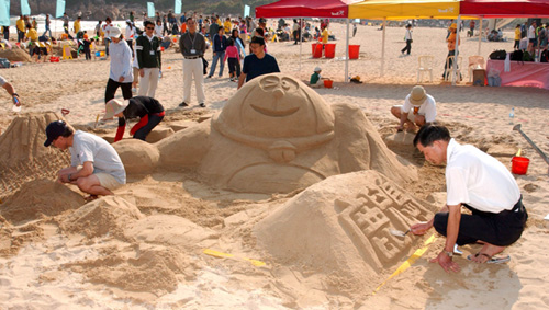 Sand sculptors from Kagoshima, Japan, working on their creation,'The Relaxing Doraemon in the Hot Spring'.